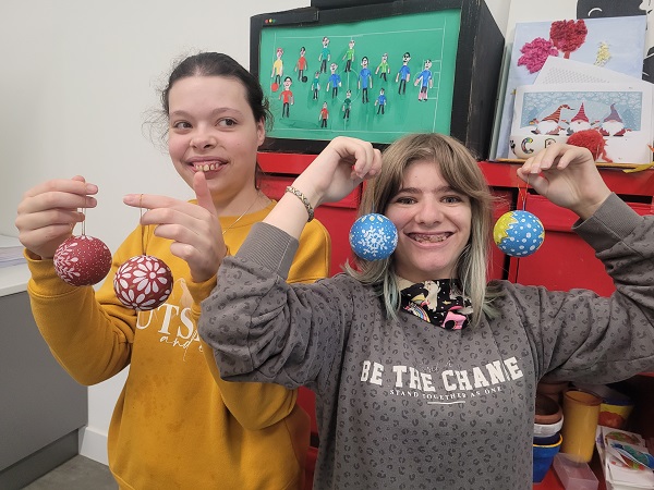 Two smiling young women hold up Christmas baubles